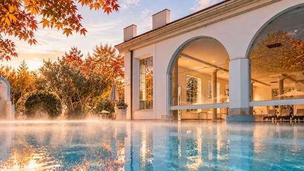 A swimming pool with clear water, surrounded by a building with large windows and an arched entrance. - Bellavista Terme Resort & Spa (Montegrotto Terme)