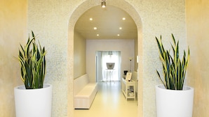A hallway with a white bench, potted plants, and a coffee machine on a white stand. - Bellavista Terme Resort & Spa (Montegrotto Terme)