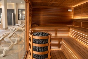 A sauna with wooden benches and a central fire pit, surrounded by a tiled floor and a glass partition. - Bellavista Terme Resort & Spa (Montegrotto Terme)