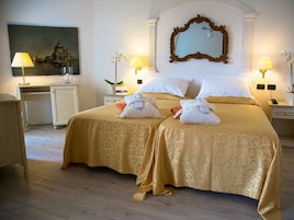 A hotel room with two beds, a desk, a chair, a lamp, a mirror, and a painting on the wall.