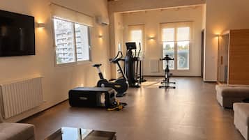 Un vaste espace de vie doté d’un téléviseur à écran plat, d’un équipement de musculation et d’une grande fenêtre offrant une vue sur l’extérieur.