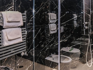 A modern bathroom with a black marble backsplash, a glass shower enclosure, and a toilet with a bidet attachment. - Bellavista Terme Resort & Spa (Montegrotto Terme)