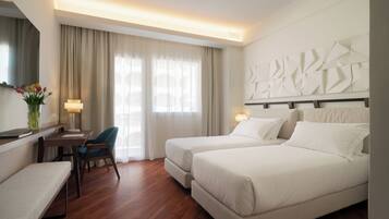 A hotel room with two beds, a desk with a chair, a lamp, and a vase with flowers.