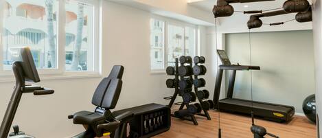 Un gimnasio con equipo de ejercicio, una cinta de correr y ventanas con vistas a edificios.