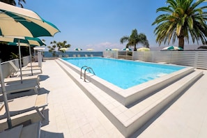 Piscina retangular com superfície de água azul límpida, rodeada por um deck de azulejos brancos.