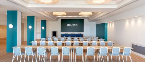 A conference room with a large screen displaying 'DELFINO TARANTO' and multiple rows of chairs.