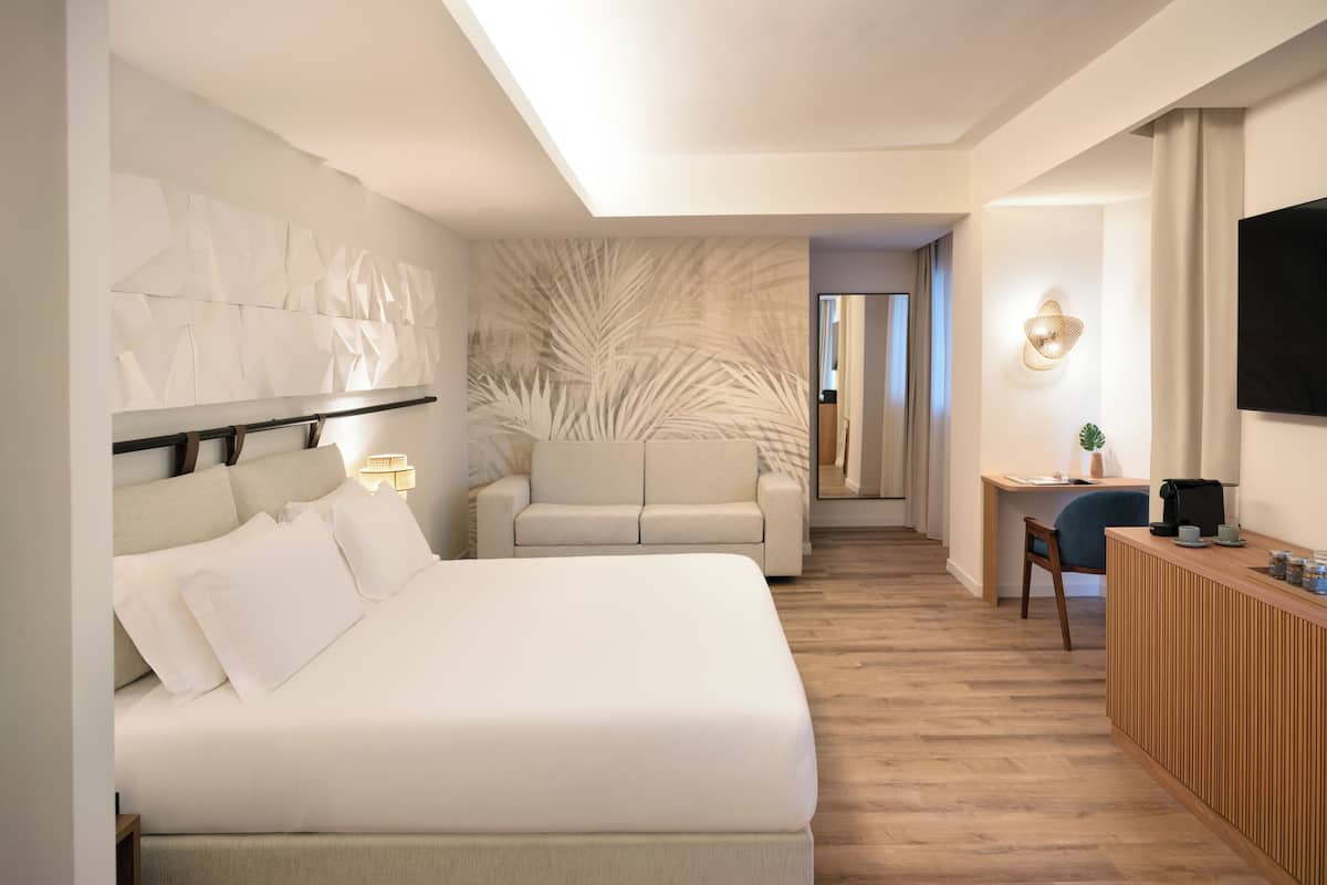 Une chambre d’hôtel moderne, dotée d’un grand lit, d’un canapé, d’un bureau avec une chaise et d’un téléviseur fixé au mur.