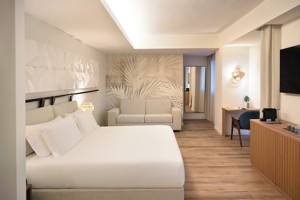 Habitación de hotel moderna con una cama grande, un sofá, un escritorio con una silla y un televisor montado en la pared.