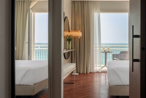 Habitación de hotel con dos camas, una mesita con lámpara y vista al mar.