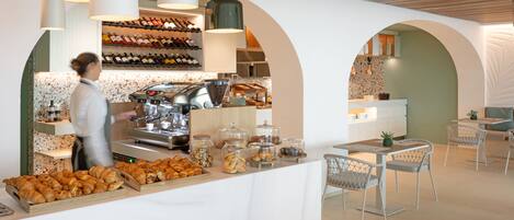 A modern cafe with a counter displaying pastries and coffee, a coffee machine, and a wine rack in the background.