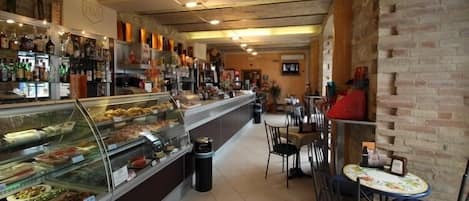 Un café con pared de ladrillo, una vitrina con pasteles y una zona de estar con mesas y sillas.