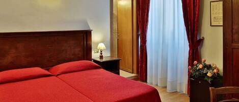Una habitación de hotel con una cama grande, una mesita de noche con lámpara, un armario de madera y una puerta que da al baño.