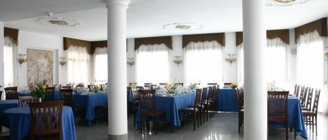 A spacious dining hall with high ceilings, white columns, and blue tablecloths.