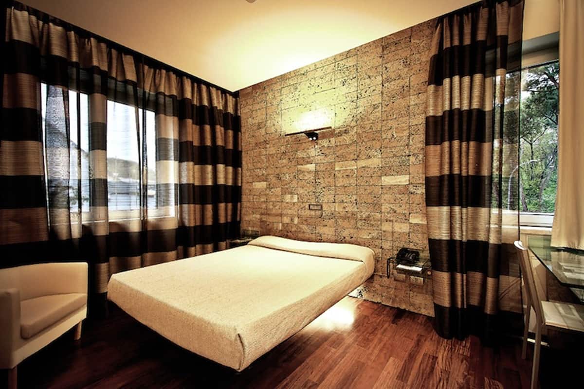 A room with a bed, a chair, a desk, and a stone wall.