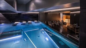 A modern indoor pool with a clear water surface, lounge chairs, and a stone wall backdrop. - Hotel All Time Relais & Sport (Rome)