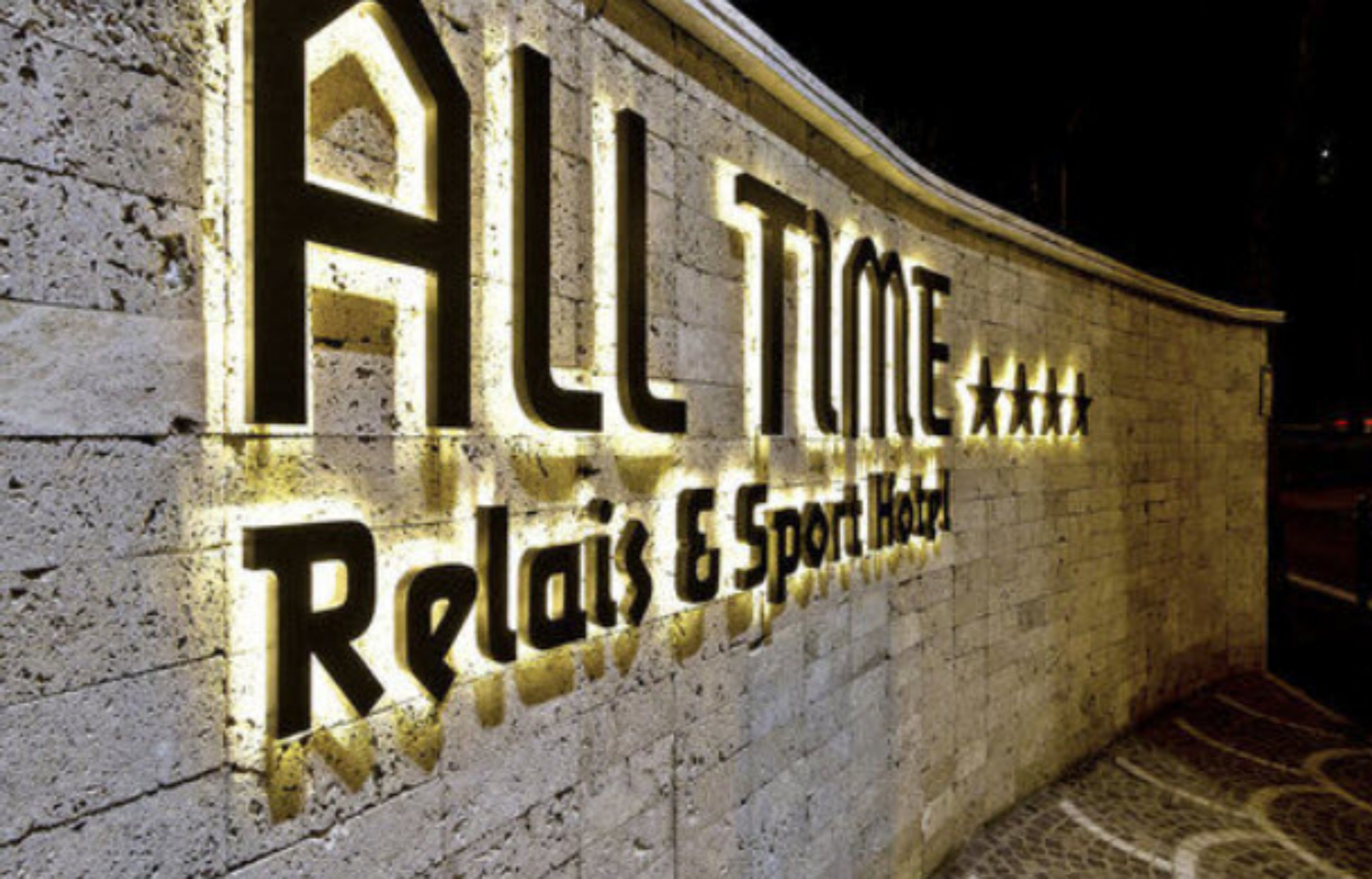 Una pared con iluminación que muestra el texto "ALL TUNE Relax & Sport Hotel".