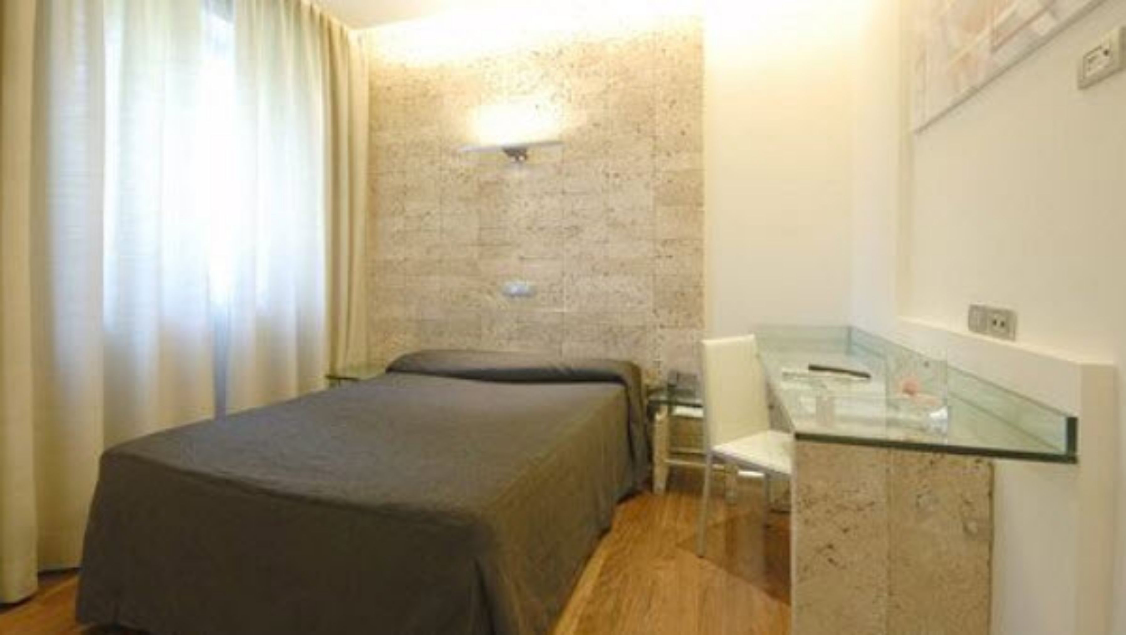Una habitación de hotel con cama, escritorio con silla y un separador de vidrio.