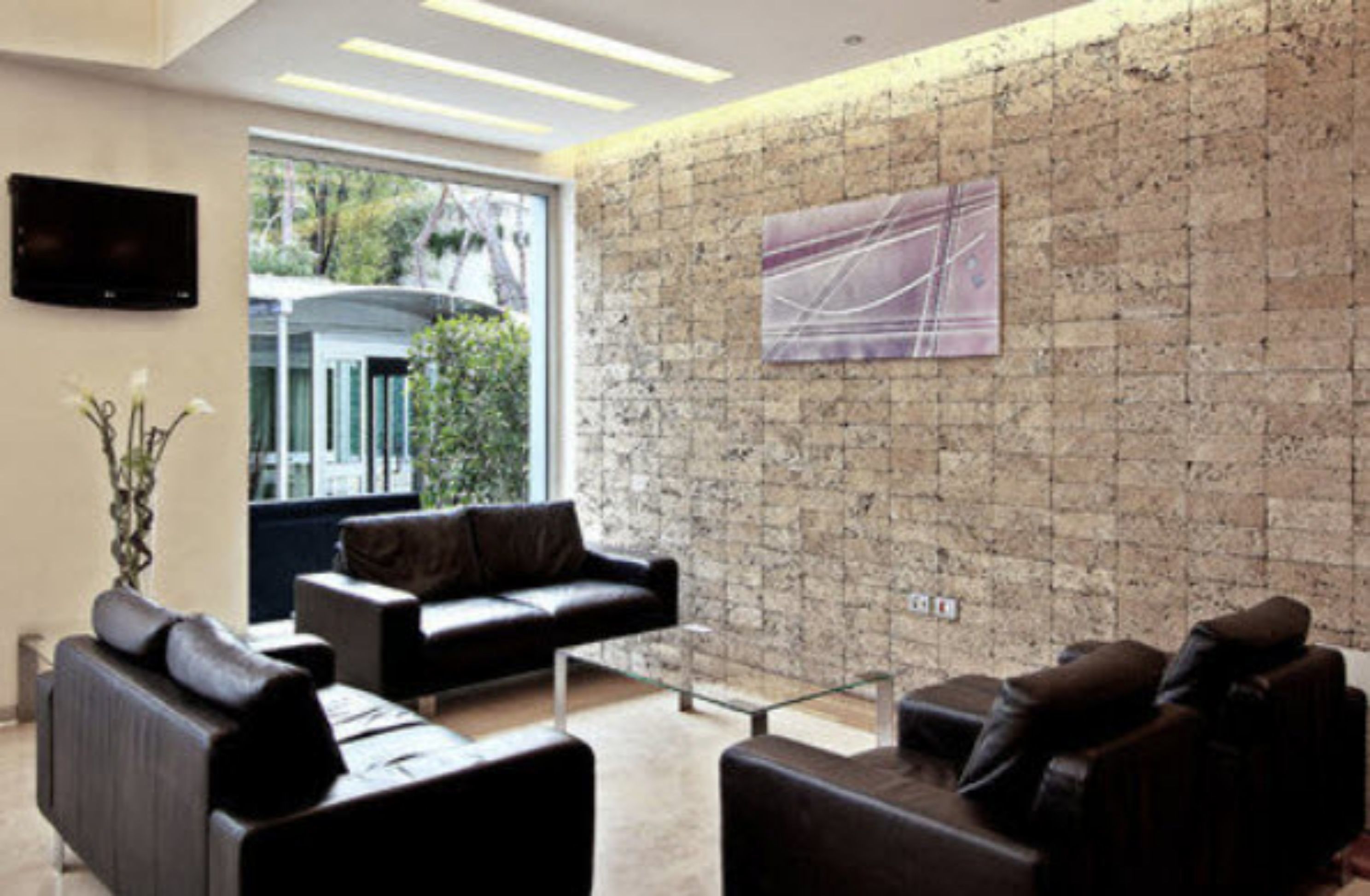 A modern living room with a stone wall, a flat-screen TV mounted on the wall, and a large window offering a view of greenery outside.