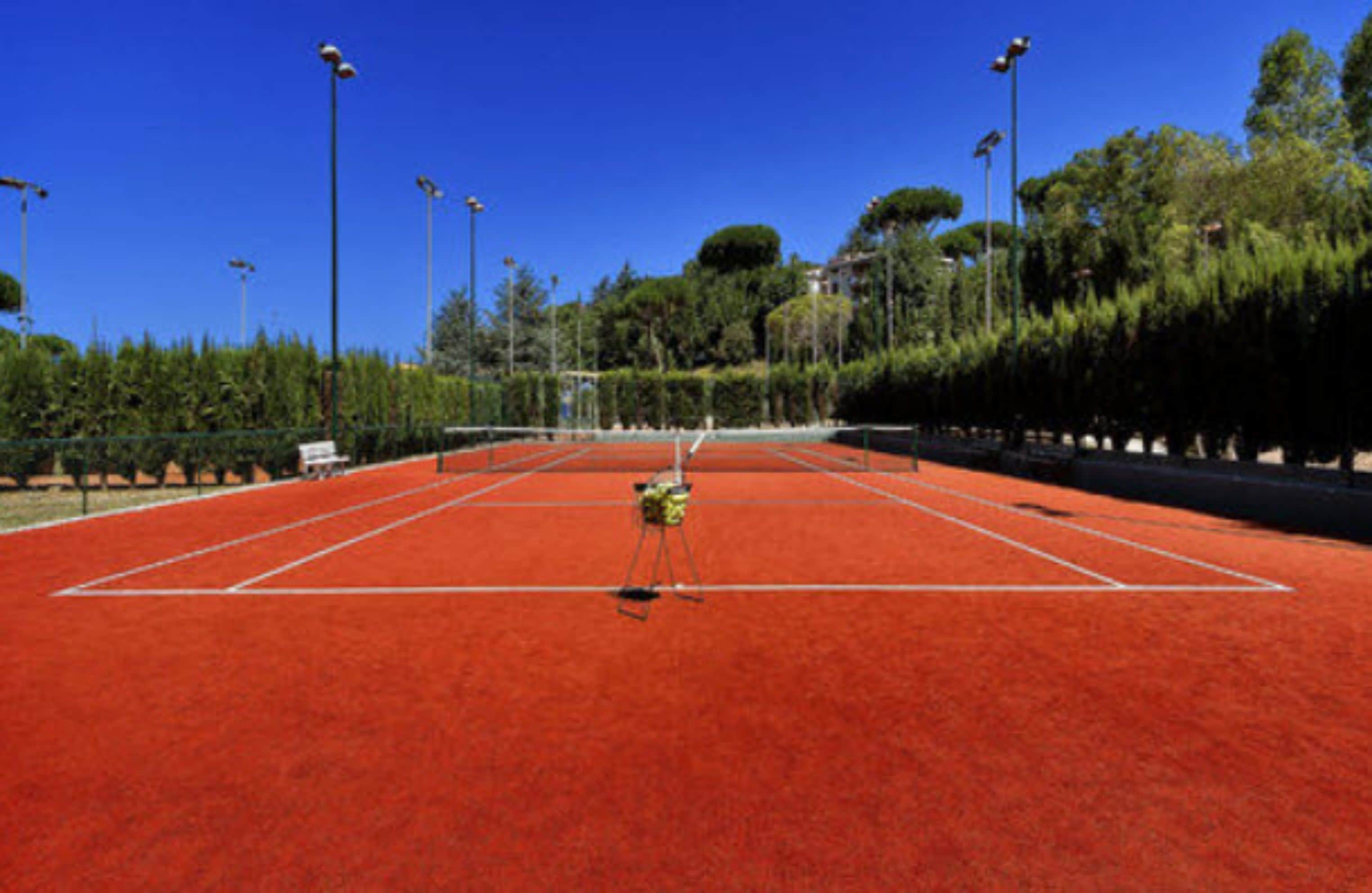 A tennis court with a net, surrounded by trees and street lamps.