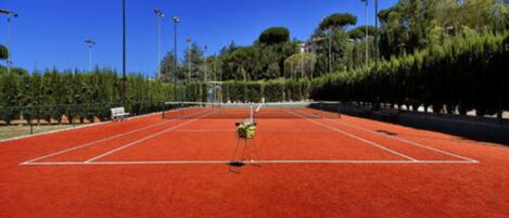A tennis court with a net, surrounded by trees and street lamps.