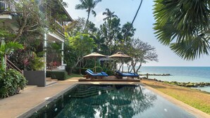 A pool area with lounge chairs and umbrellas, surrounded by tropical vegetation and a view of the sea. - Napasai Samui (Koh Samui)