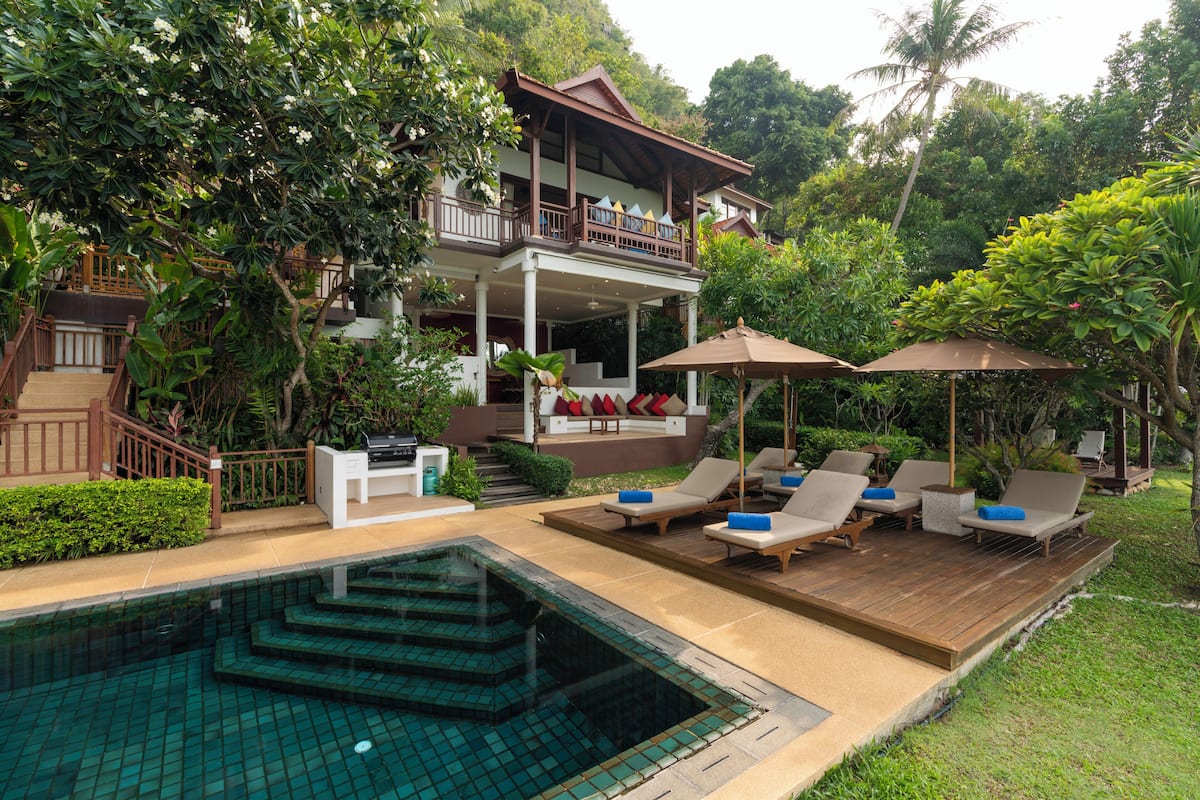 A two-story building with a pool, lounge chairs, and a covered deck.