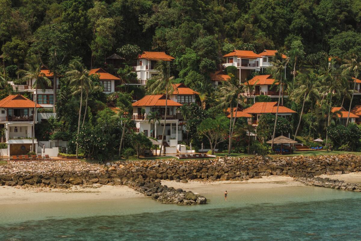 A coastal resort with multiple buildings, a rocky shoreline, and clear turquoise water.