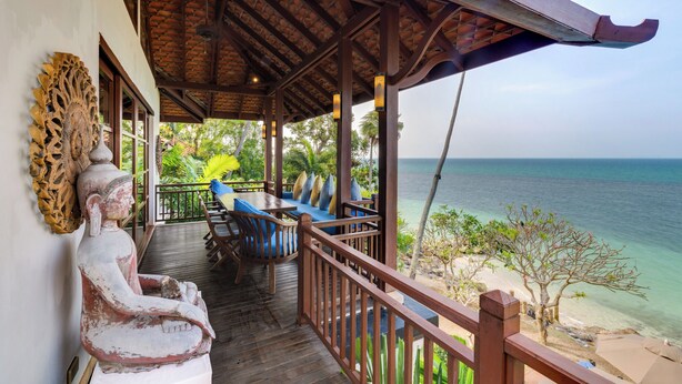 A wooden deck with a Buddha statue, a table with chairs, and a view of the ocean. - Napasai Samui (Koh Samui)