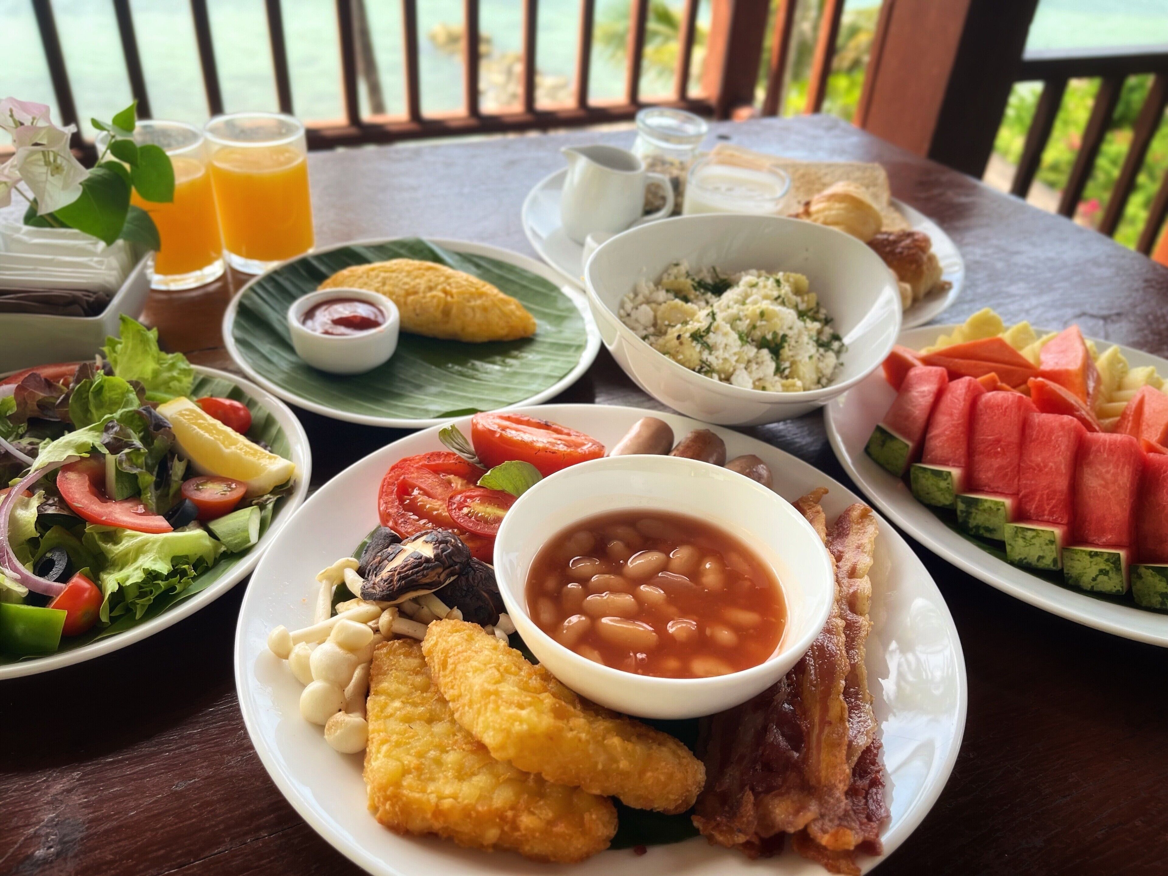 A table with various dishes including salad, beans, bacon, and fruit.