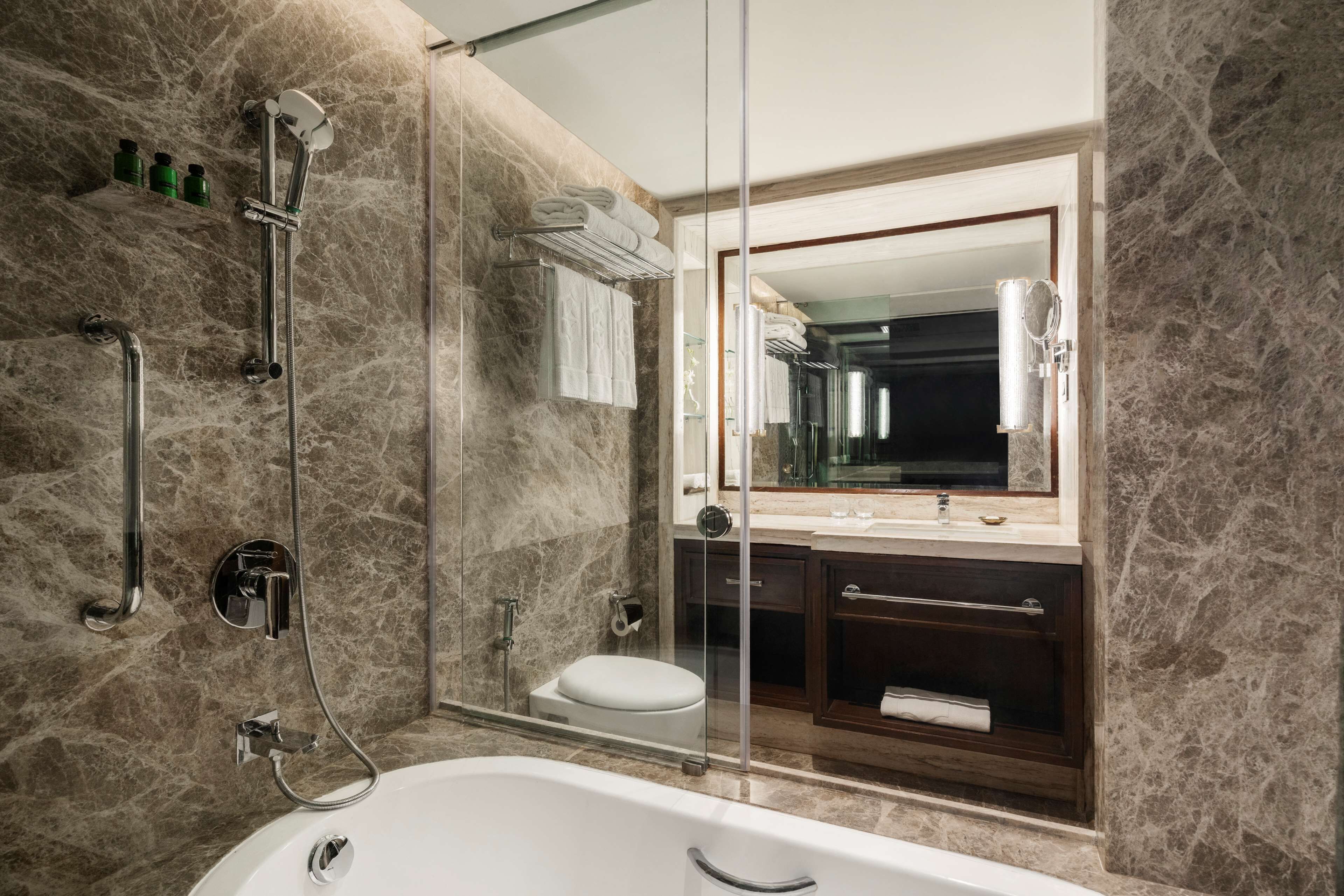 Ein modernes Badezimmer mit einer gläsernen Duschkabine, einer weißen Badewanne, einem dunklen Holzwaschtisch und einem großen Spiegel über dem Waschbecken.