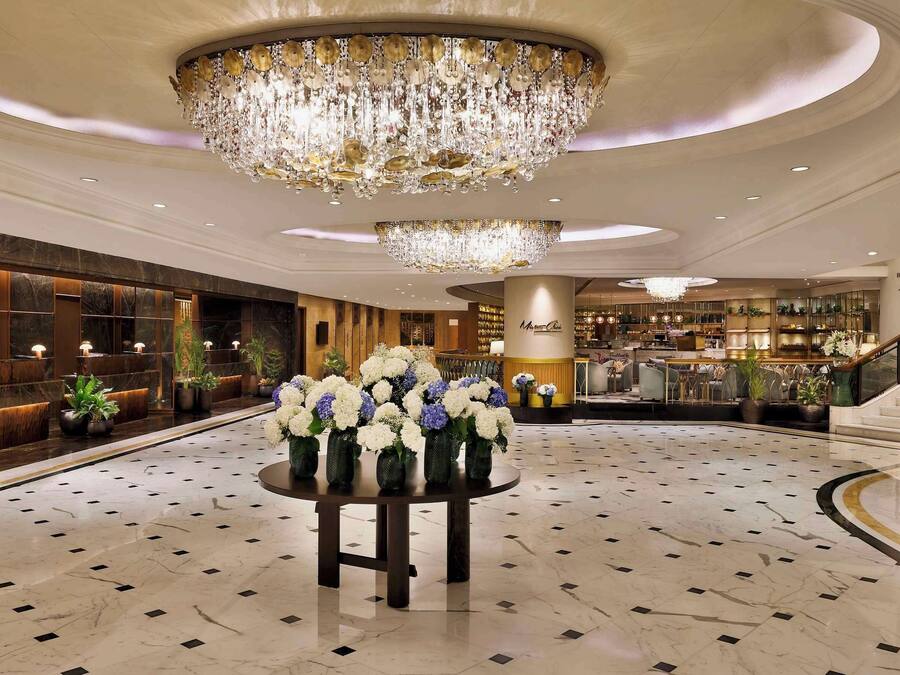 A spacious lobby with a grand chandelier, a reception desk, and a staircase leading to the upper floors.