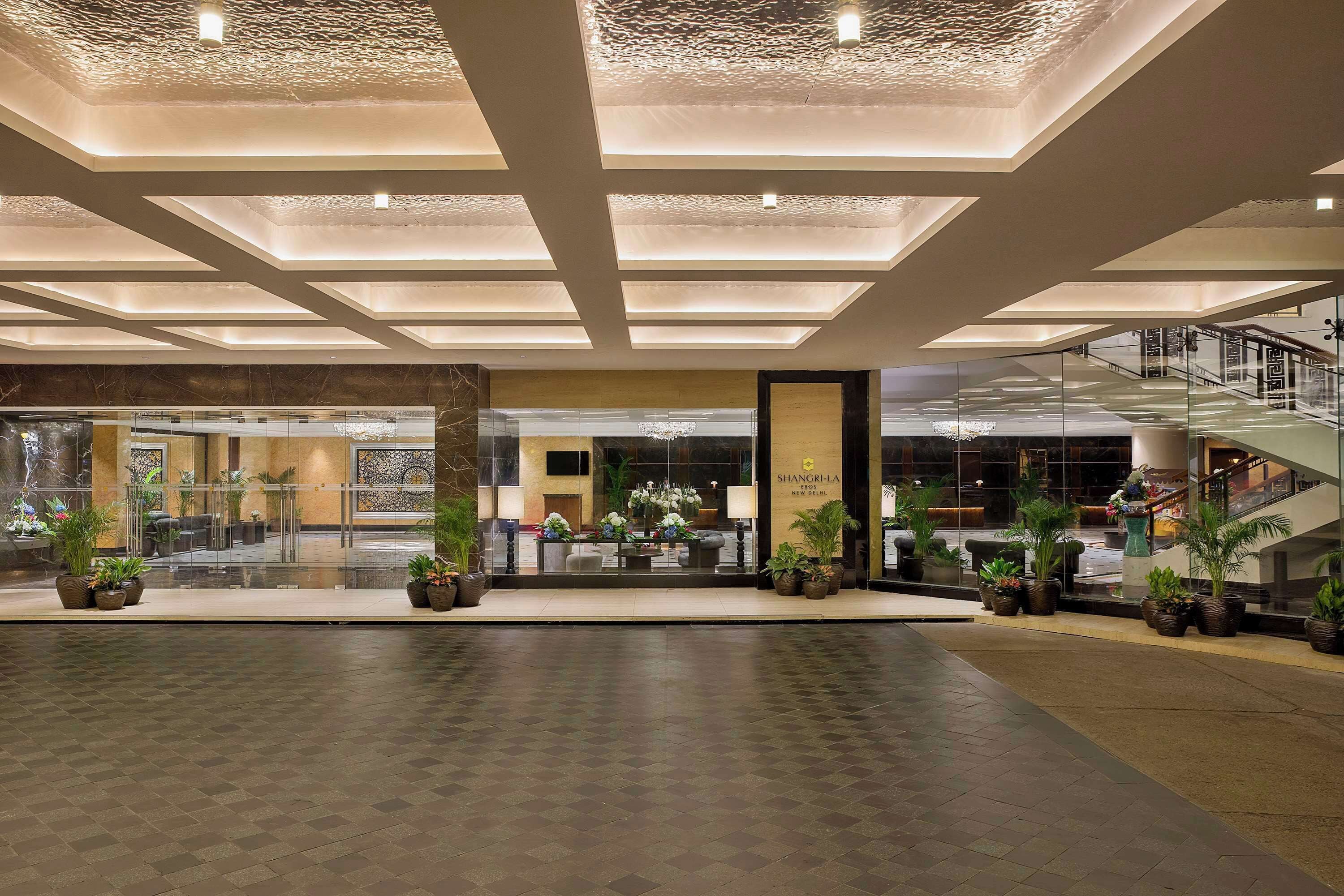 A spacious lobby with a modern ceiling design, a central seating area with plants, and a staircase on the right.