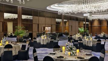A banquet hall with round tables, black chairs, and chandeliers.