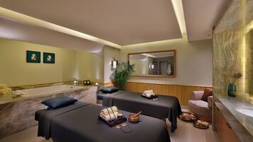 A spa room with two massage tables, a large mirror, and a plant.