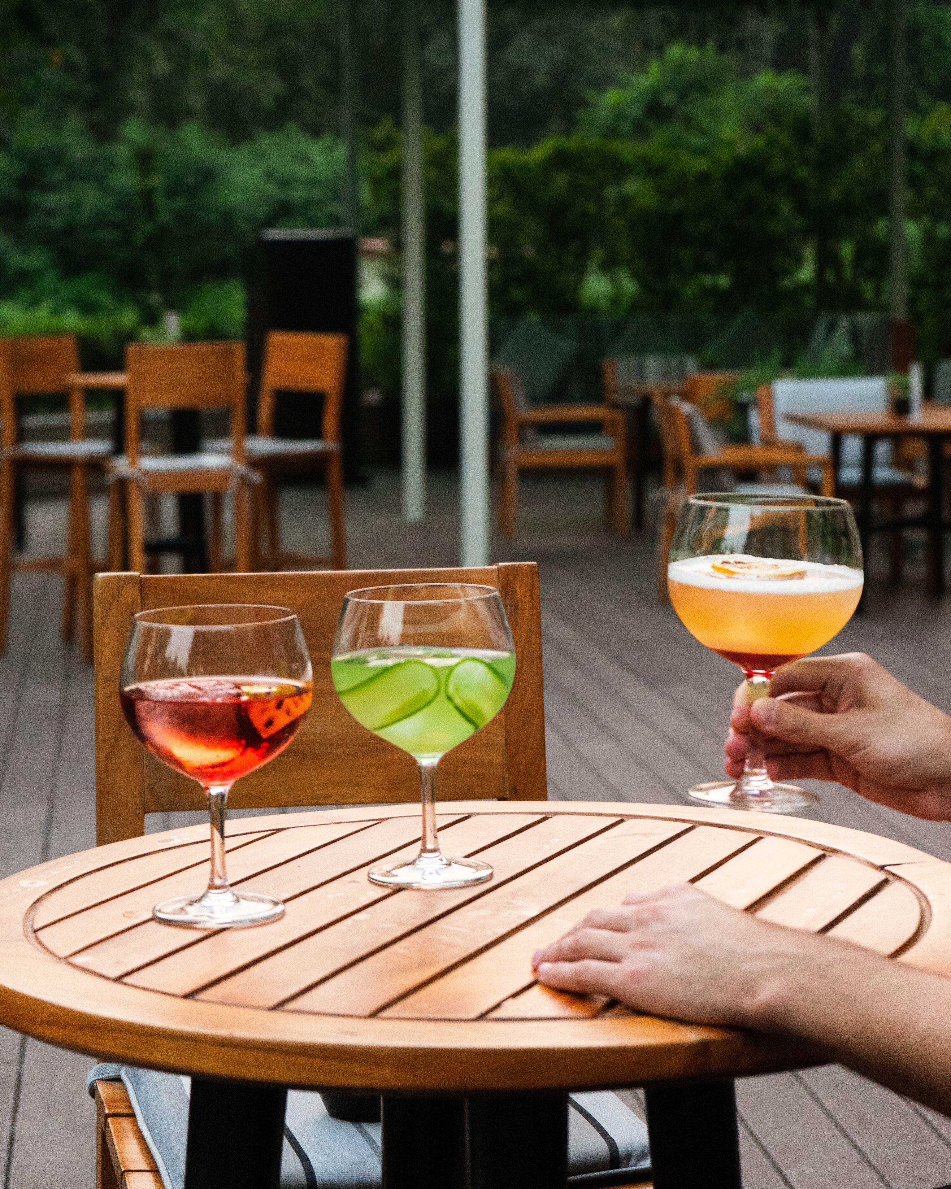 Una mesa de madera con tres vasos de bebidas: uno con un líquido rojo, otro con uno verde y un tercero con uno naranja.