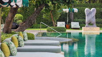 Ein Poolbereich mit Skulptur, Sitzgelegenheiten und einem gepflegten Garten.