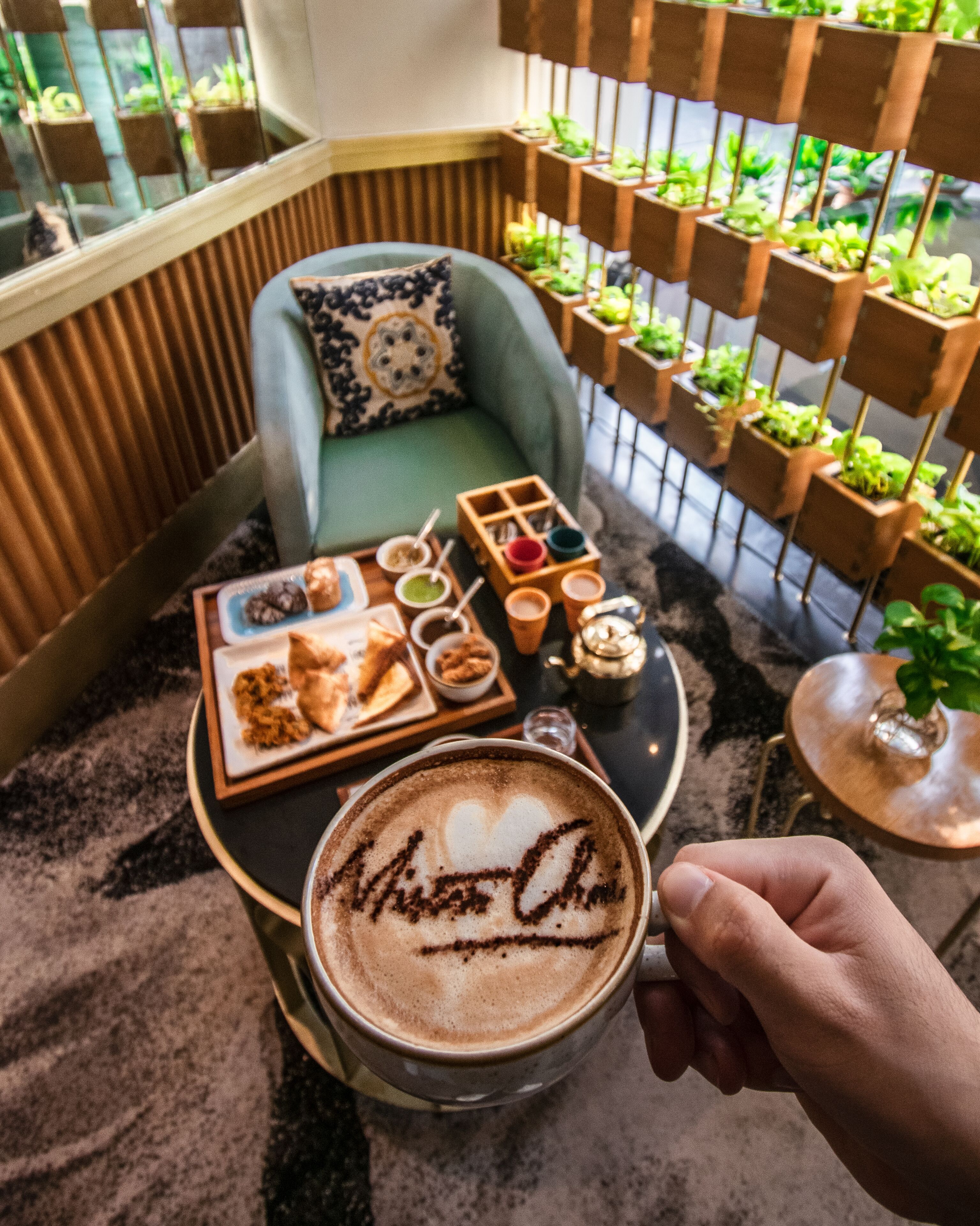 Eine gemütliche Sitzecke mit gepolstertem Sessel, einem kleinen Tisch mit Speisen und Getränken und einer Kaffeetasse mit Latte-Art.