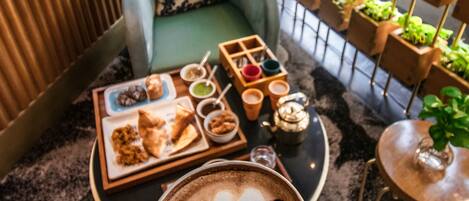 A cozy seating area with a cushioned chair, a small table with a tray of food and drinks, and a coffee cup with latte art.
