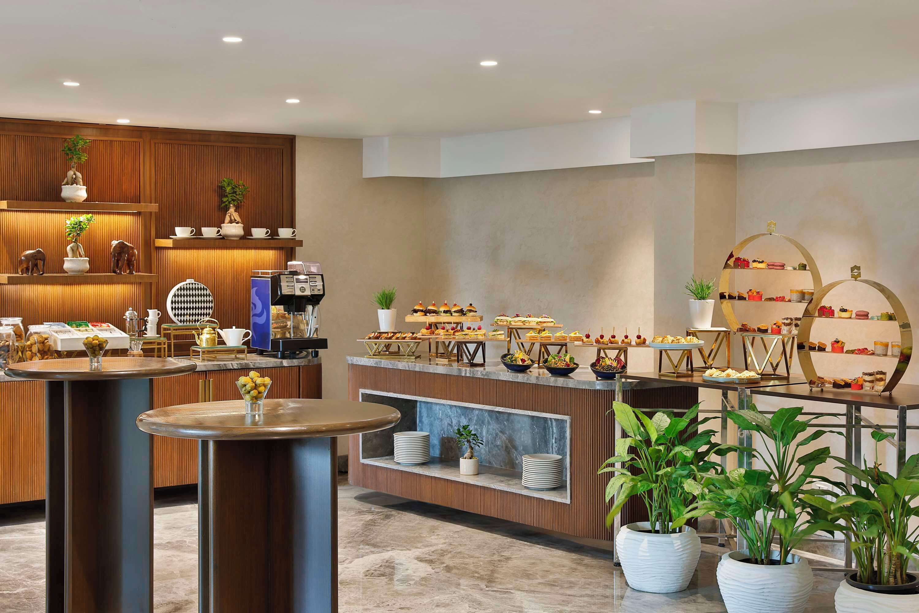A buffet area with various food items, a coffee machine, and decorative plants.