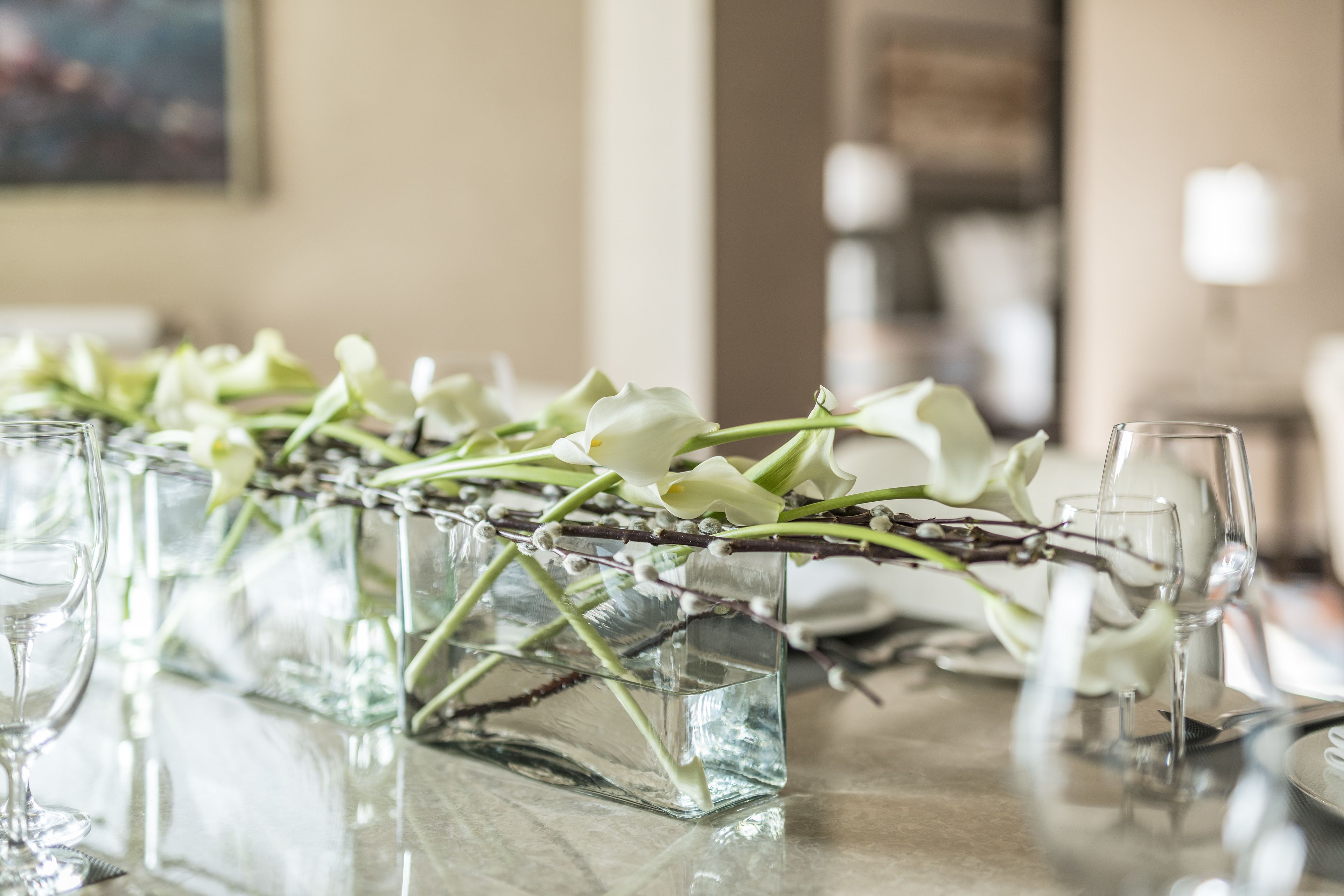 A table with a floral arrangement in a glass vase, surrounded by empty wine glasses and plates.
