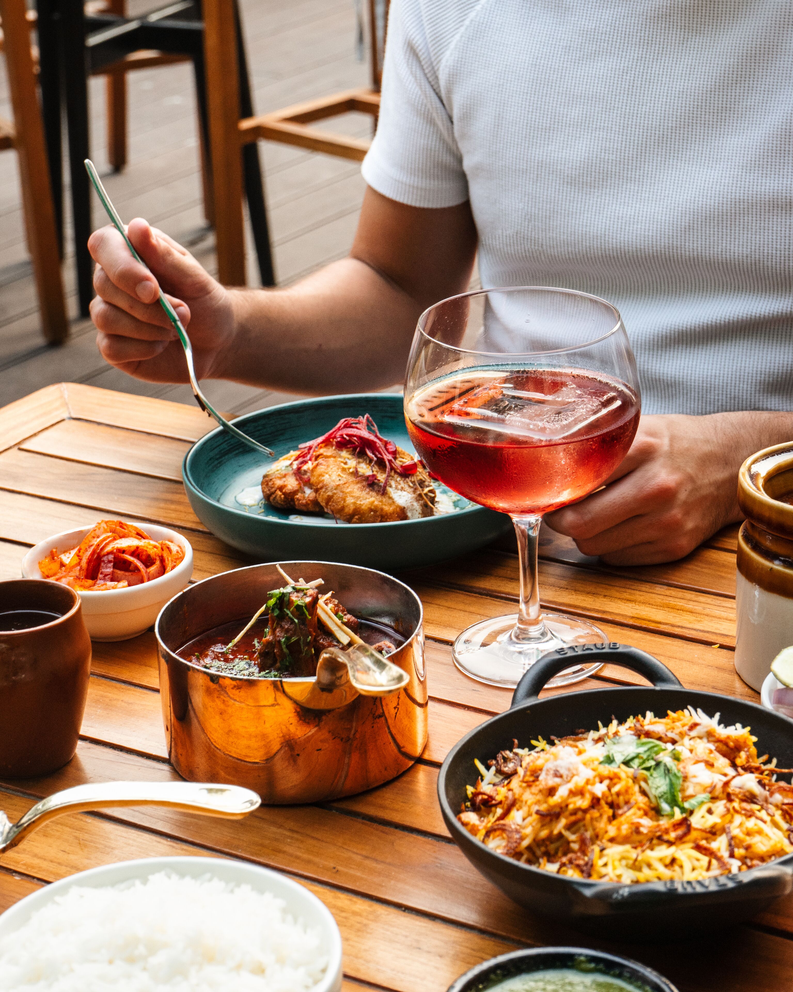 A dining table with various dishes, including a bowl of rice, a pan of food, and a glass of red drink.
