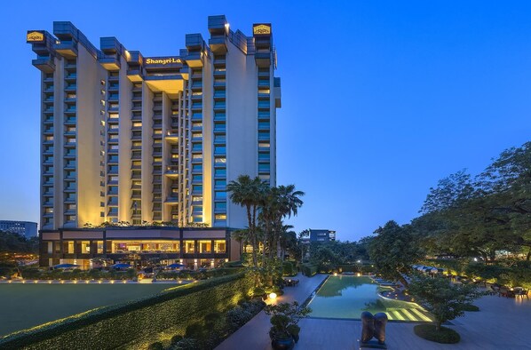 A high-rise hotel with multiple floors, a swimming pool, and well-maintained gardens.