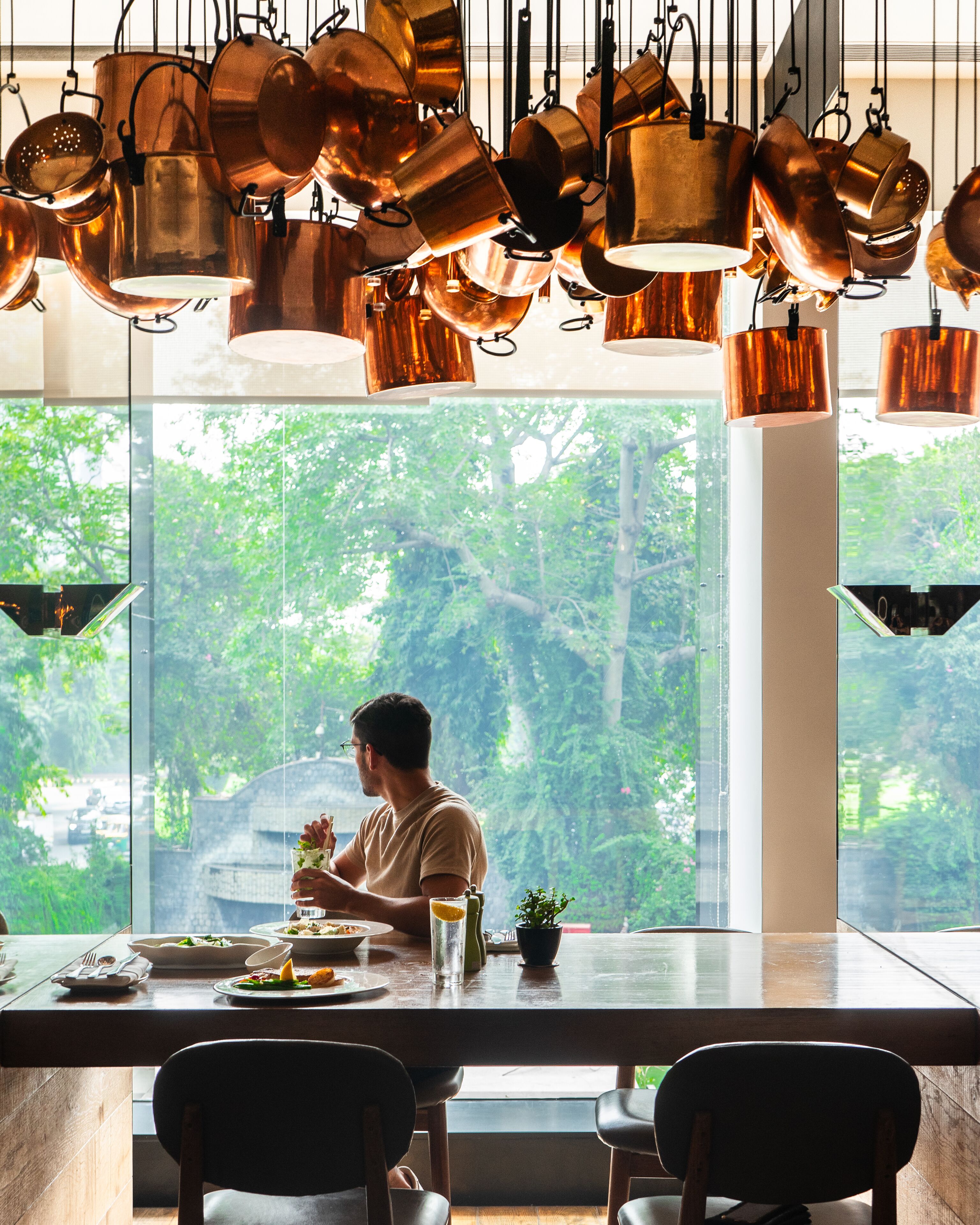 A dining area with a large window, a table with chairs, and hanging copper pots.