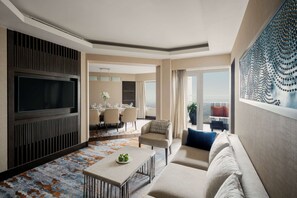 A modern hotel room with a flat-screen TV, a dining area, a sofa, and a large window with a view.