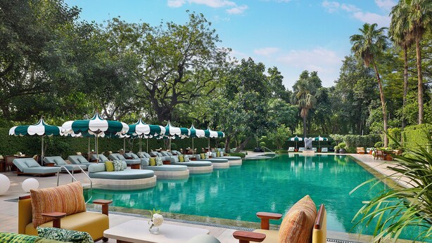 A pool area with lounge chairs and umbrellas, surrounded by trees. - Shangri-La Eros, New Delhi (New Delhi)