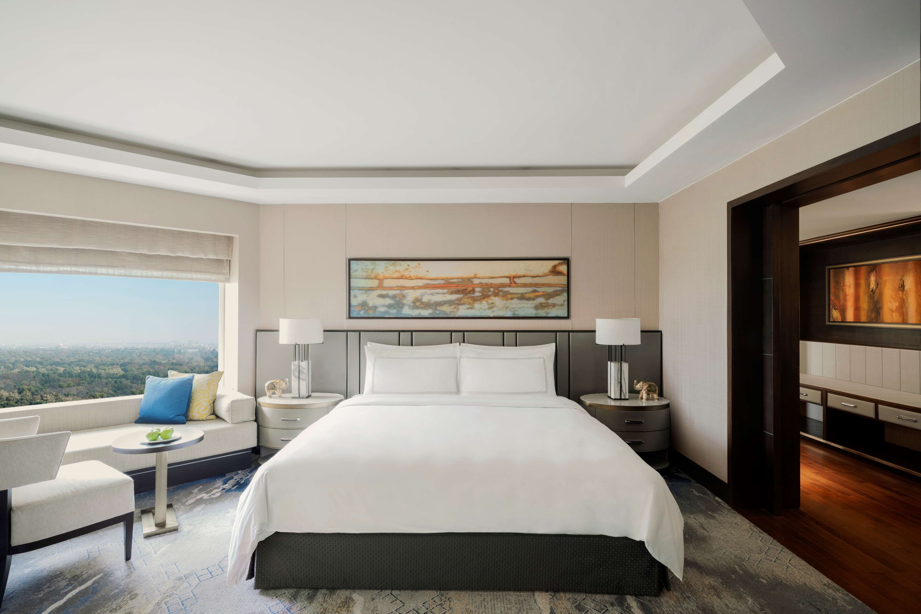 A hotel room with a large bed, two bedside tables with lamps, a sofa with a view, and a painting on the wall.