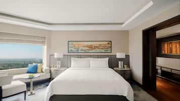 A hotel room with a large bed, two bedside tables with lamps, a sofa with a view, and a painting on the wall.