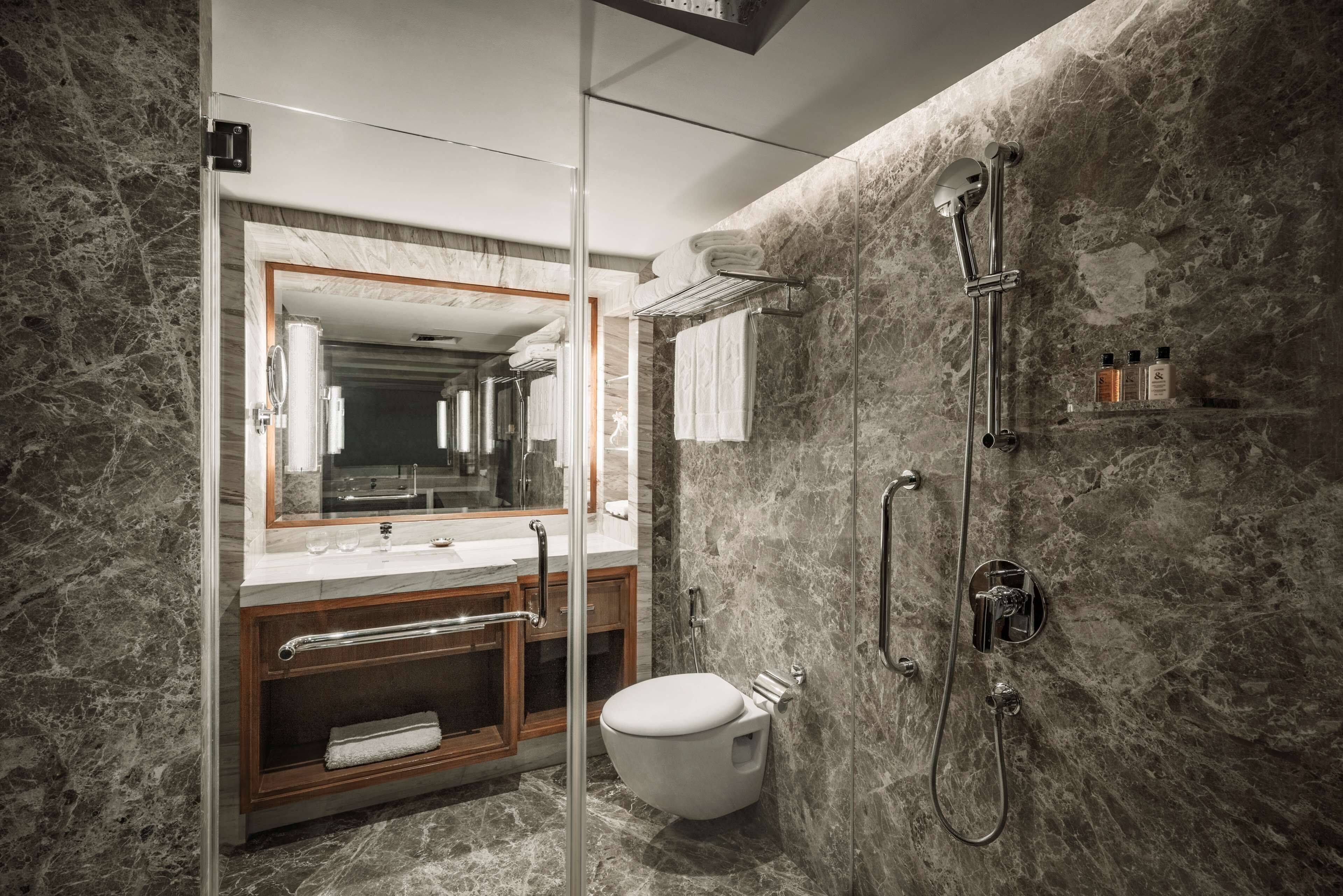 Un baño moderno con pared de mármol, cabina de ducha de vidrio, tocador de madera y un inodoro.