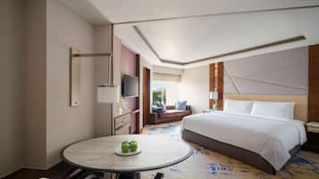 A hotel room with a large bed, a round dining table with apples, a TV, and a view of the outdoors.
