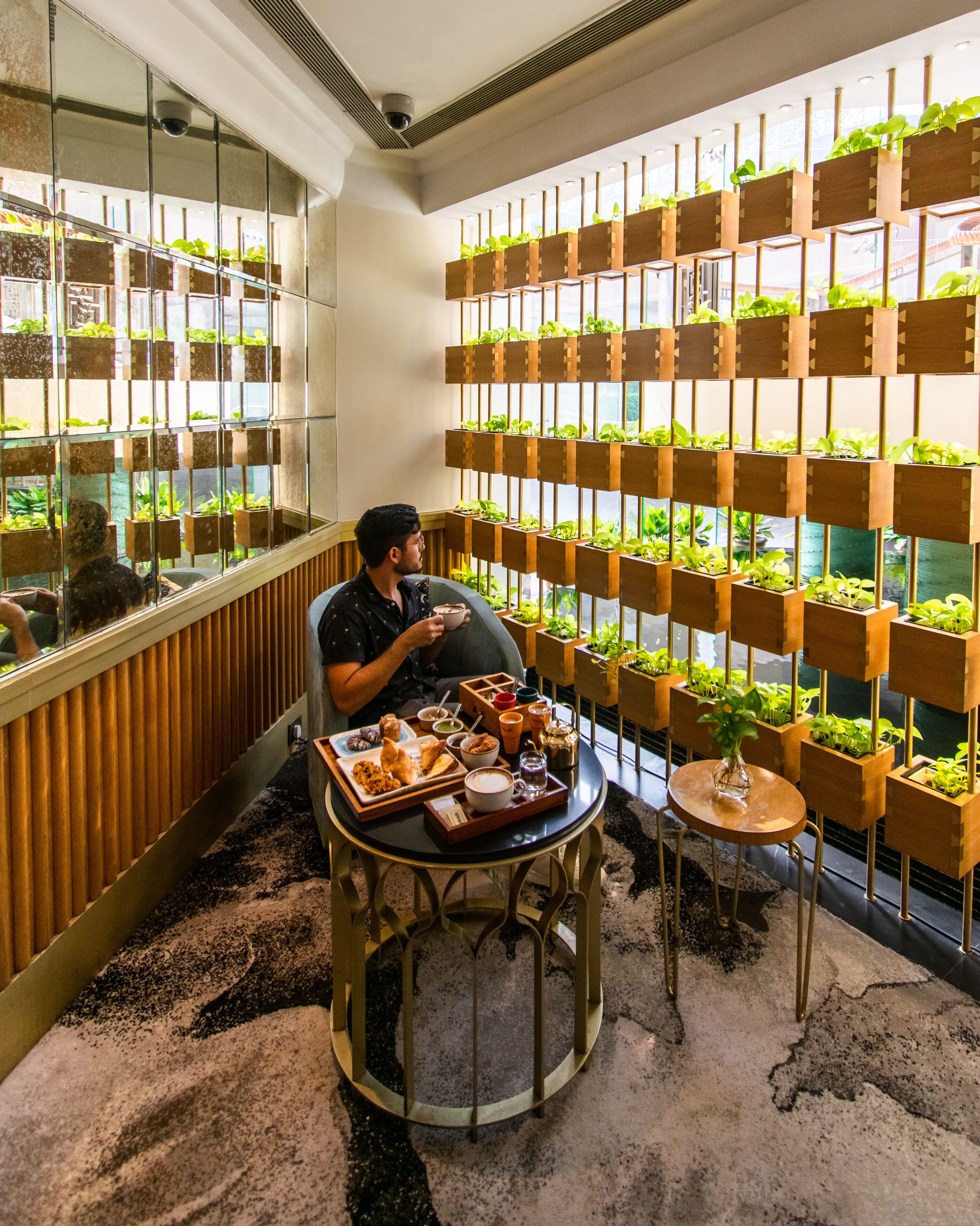 Et værelse med moderne design, hvor et stort vindue giver udsigt til grønne omgivelser. Der er et spisebord med forskelligt mad samt et lille sofabord med en plante.
